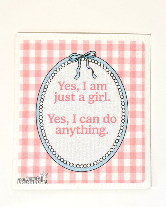 A square dish towel with a pink and white gingham pattern, featuring a central oval design with the text 'Yes, I am just a girl. Yes, I can do anything.