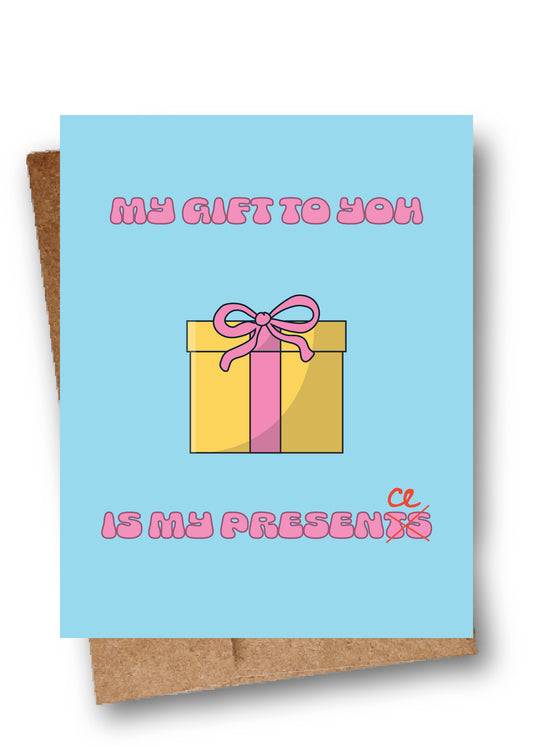 A square greeting card with a light blue background, featuring a cartoon gift box with pink ribbon and the text 'MY GIFT TO YOU IS MY PRESENT' in pink bubble letters. A brown kraft envelope is partially visible behind the card.