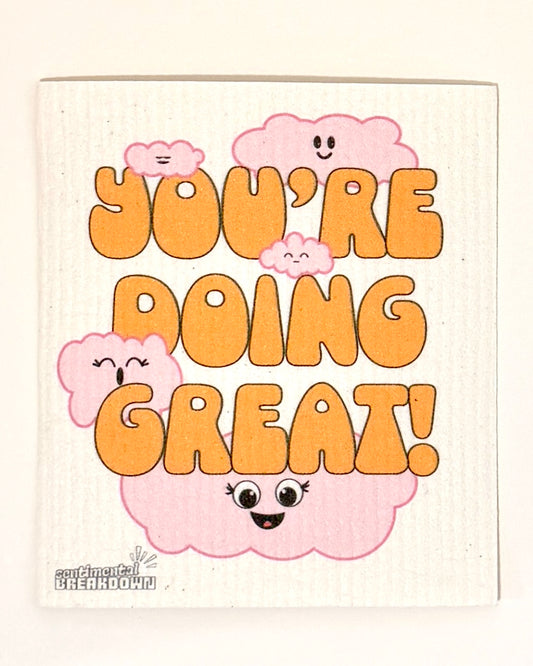 A square decorative dish towel or napkin with a white ribbed background, featuring the phrase 'YOU'RE DOING GREAT!' in bold orange letters, surrounded by cute pink smiling cartoon clouds.